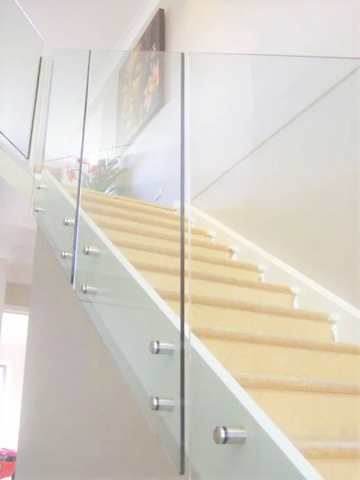 Baranda de vidrio templado con botones de acero inoxidable en una escalera con escalones de madera - obra de J&N Aluminio en Neuquén