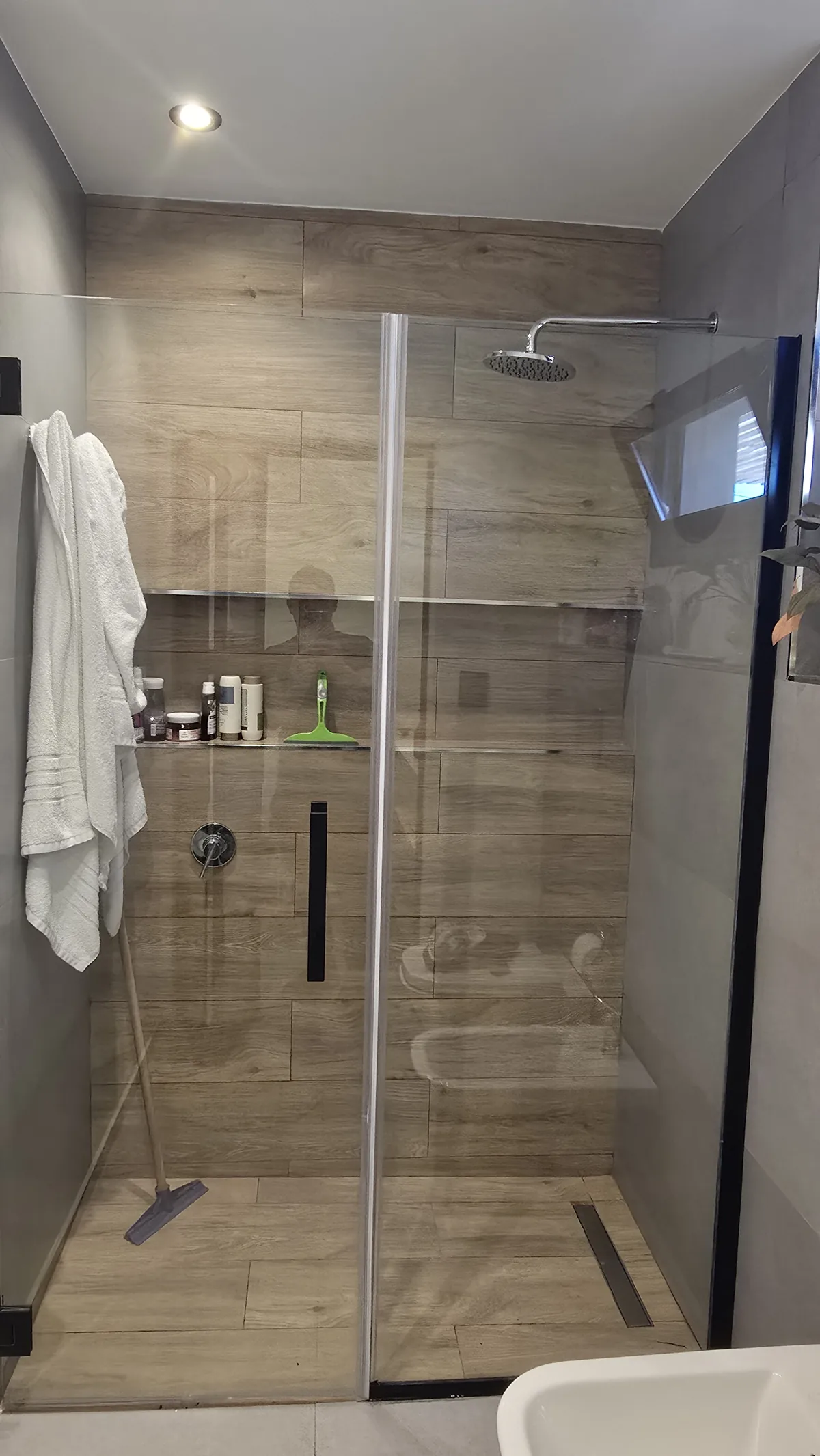Mampara corrediza de vidrio templado con herrajes negros en baño revestido en madera - JN Aluminio Neuquén