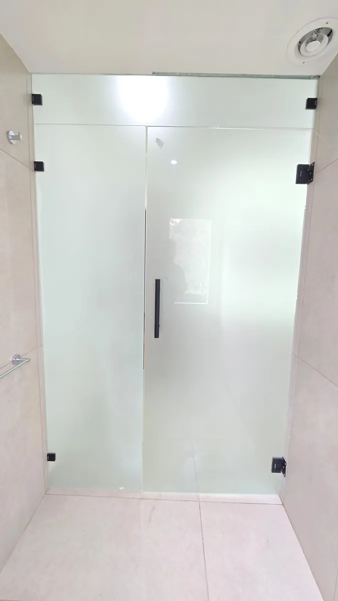 Mampara rebatible con paño fijo, sistema frameless con bisagras y clips negros y vidrio templado Blindex esmerilado - obra de J&N Aluminio en Neuquén