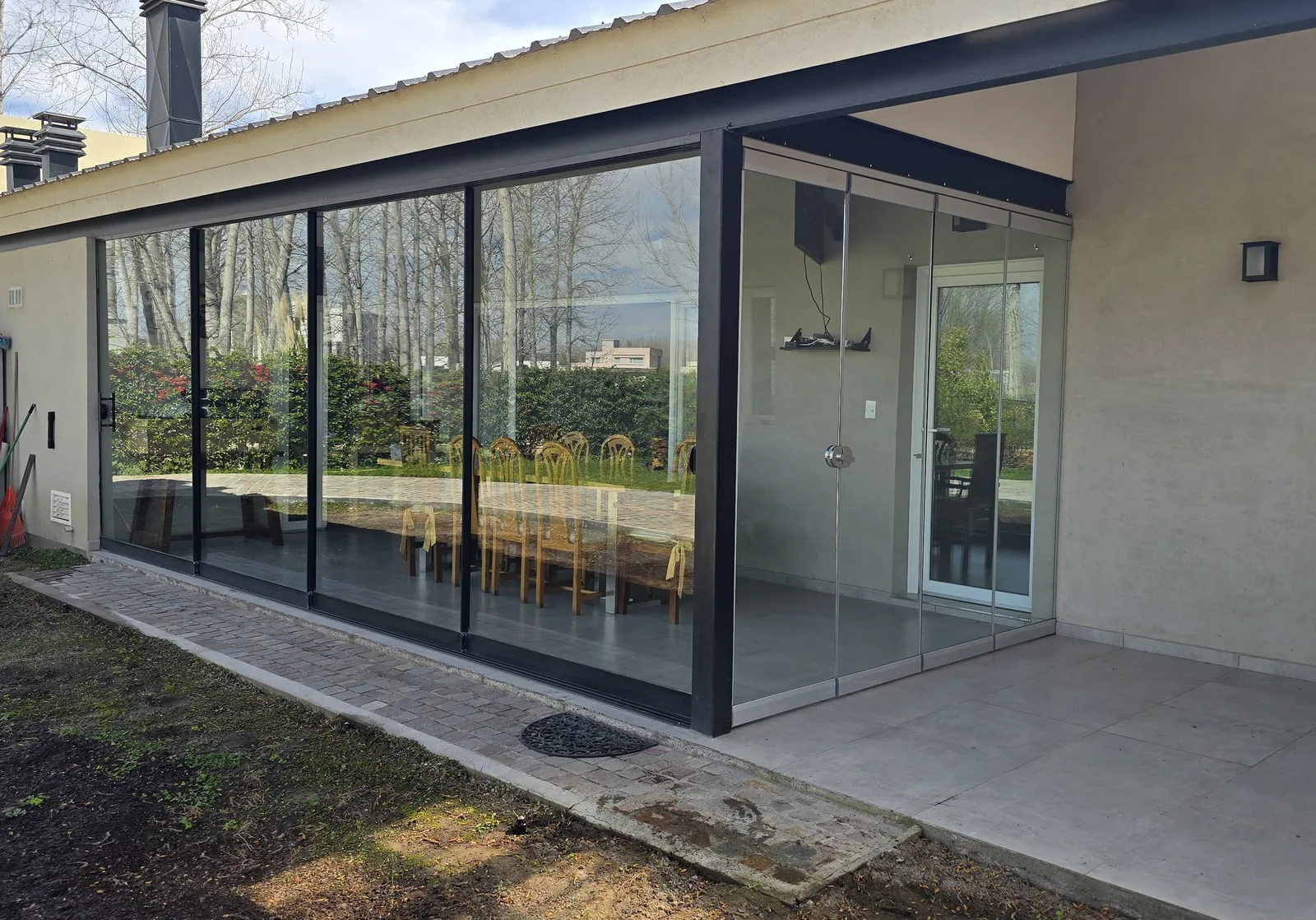 Galería cerrada con dos sistemas de vidrio: cerramiento deslizante de perfilería negra al frente y sistema apilable sin perfiles en el lateral - obra de J&N Aluminio en Los Canales, Plottier