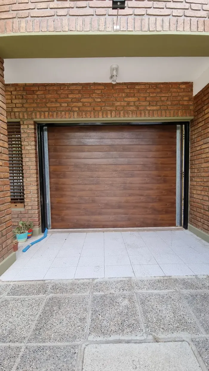 Portón enrollable símil madera instalado en frente de ladrillo visto - obra de JN Aluminio en Neuquén